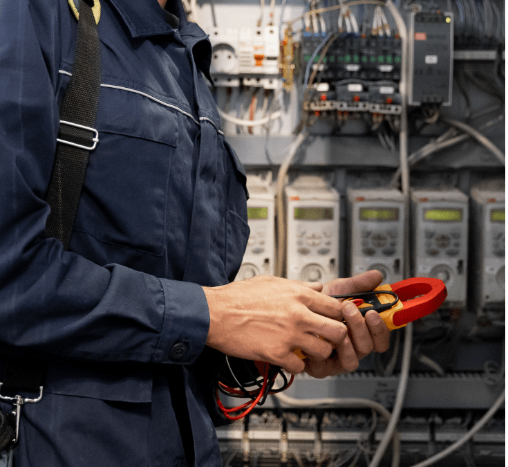Electrician wearing blue coveralls with circuit tester in industrial electrical room