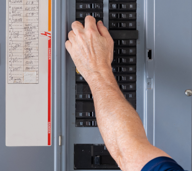 Person reaching up to electrical panel box to turn on circuit breakers