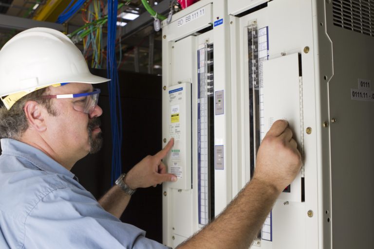 Hardhat Worker Adjusting Levels On DC Panel - finding emergency electricians